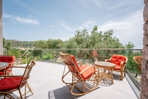 Un balcon doté de meubles en osier et d’une rambarde en verre, offrant une vue sur un paysage verdoyant.