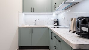 A modern kitchen with light green cabinets, a marble countertop, and stainless steel appliances including a kettle and a coffee maker.