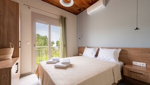 A bedroom with a large bed, a wooden headboard, a bedside table, a nightstand, a hanging light, and a view of the outdoors through a sliding door.