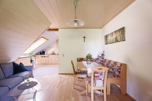 Ein modernes Wohnzimmer mit einer Couch, einem Esstisch mit Stühlen, einem Deckenventilator und einer Küche im Hintergrund.