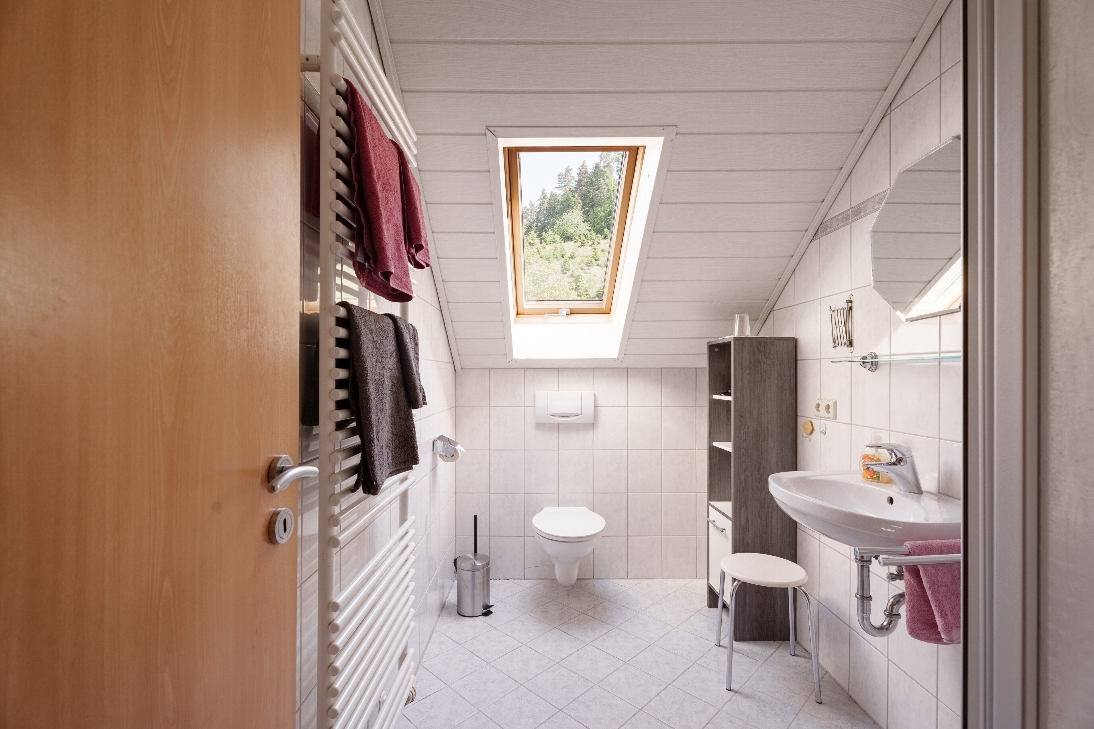 A compact bathroom with a skylight, a toilet, a sink, and a small stool.
