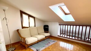 A spacious room with a wooden parquet floor, a white sofa, a small rug, a floor lamp, and a skylight.