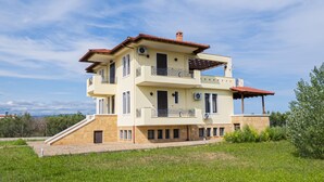 A two-story house with a flat roof, a balcony on the upper floor, and a small staircase leading to the entrance. - Casa Natura Rodanthi by Rentals Pro (Nea Propontida)