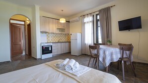 A hotel room with a bed, a dining table with chairs, a kitchen area with appliances, and a TV on the wall. - Casa Natura Rodanthi by Rentals Pro (Nea Propontida)