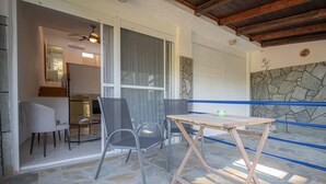 A stone-floored patio with a table and chairs, a ceiling fan, and a view of the interior through a glass door.