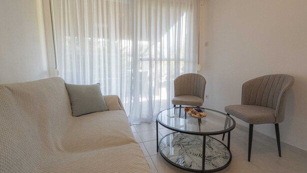 A living room with a beige sofa, two armchairs, and a glass coffee table.