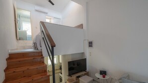 A modern living room with a wooden staircase, a flat-screen TV, a small table, and a sofa.
