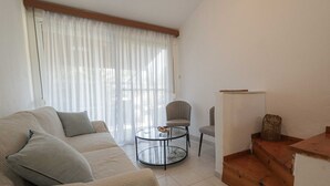 A living room with a beige sofa, two armchairs, a glass coffee table, and a wooden staircase.