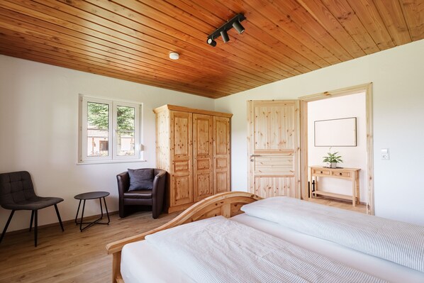 Quarto com teto de madeira, uma cama, uma cadeira, uma mesinha e armários de madeira.