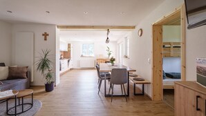 Et moderne interiør med spiseplads, sofa, en potteplante og en synlig træbjælke i loftet.