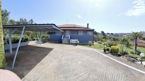Ein Haus mit überdachter Terrasse, umzäunter Garten und Blick auf die umliegende Landschaft.