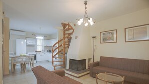 A living room with a sofa, a coffee table, and a fireplace. There is a staircase leading to a kitchen area. - Eria Home by Rentalspro - Trikorfo Halkidiki (Polygyros)