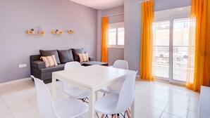 A modern living room with a grey sofa, white dining table, and orange curtains. - Harmony Apartment 4 by Rentalspro (Kassandra)
