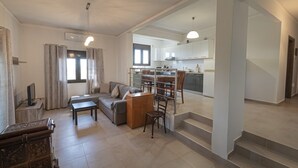 A modern living room with a sofa, coffee table, and TV, connected to a kitchen with white cabinets and a dining area. - Villa Elva by Rentalspro (Sithonia)