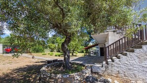 A stone-walled garden with a tree, a staircase, and a building in the background. - Villa Elva by Rentalspro (Sithonia)