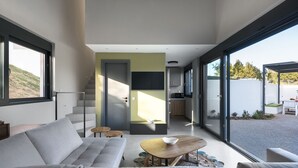 A modern living room with a sofa, coffee table, and a view of the outdoors through large windows. - Theeta Elia Villa - Metamorfosi Halkidiki (Sithonia)