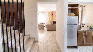Un intérieur moderne comprenant un escalier, un espace de vie avec des canapés et une cuisine équipée d’un réfrigérateur.
