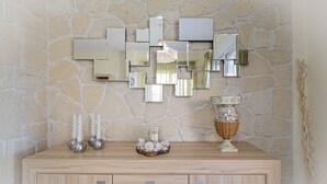 A wooden cabinet with multiple drawers against a stone wall, decorated with mirrors, candles, and a vase. - Eternal Blue by Rentalspro-hanioti Halkidiki (Kassandra)