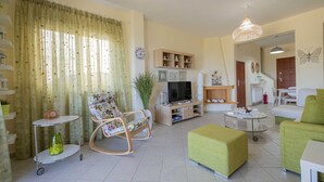 A spacious living room with a television, green ottoman, and a rocking chair. - Eternal Blue by Rentalspro-hanioti Halkidiki (Kassandra)