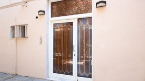 Une façade d’immeuble avec une grande porte vitrée ornée d’un cadre métallique décoratif, une petite fenêtre avec des barreaux métalliques et un luminaire fixé au mur.