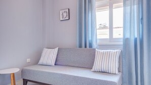 Une pièce moderne avec un canapé gris, des coussins à rayures, une petite table blanche et un tableau encadré accroché au mur.
