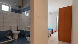 A bathroom with a toilet, sink, and shower. There is a bed in the adjacent room. - Poseidon Edge No9 by Rentalspro - Kallithea (Kassandra)