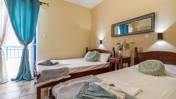 A hotel room with two beds, a nightstand, a mirror, and a window with curtains. - Poseidon Edge No5 by Rentalspro - Kallithea (Kassandra)