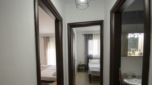 A hotel room with a bed, bedside table, and a small table with flowers. There is a bathroom with a sink and mirror. - Violeta Apartment by Rentalspro (Nea Propontida)