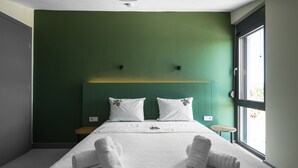 A modern hotel room with a green accent wall, a large bed with white bedding, two bedside tables, and a window providing natural light. - Theeta Pefko Villa - Metamorfosi Halkidiki (Sithonia)