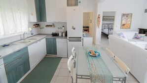 A compact kitchen with a dining area, white cabinets, a refrigerator, and a dining table with chairs. - Magdalini's Seaview House - Pefkohori (Kassandra)