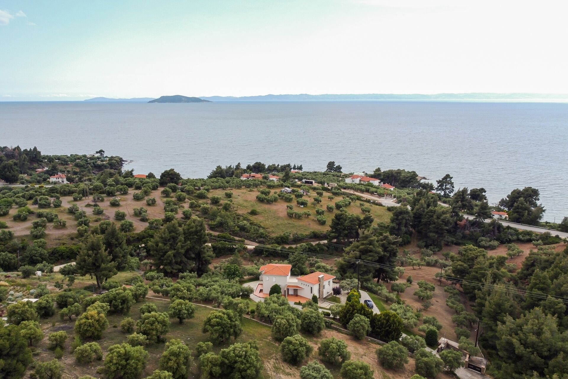 A coastal property with a central building surrounded by trees and a view of the sea.