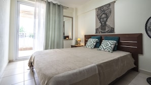 A bedroom with a large bed, a nightstand with a lamp, a window with curtains, and a wall-mounted artwork. - Tommy Seafront No 1 by Rentalspro - Nea Flogita (Nea Propontida)