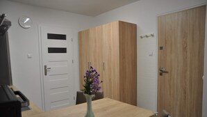 Une pièce avec une table en bois, un vase rempli de fleurs violettes, une horloge au mur et une armoire avec un miroir.