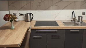 Une cuisine moderne avec des meubles de couleur sombre, une hotte en acier inoxydable, une plaque de cuisson à induction noire, un évier avec un robinet et un vase rempli de fleurs posé sur le plan de travail.