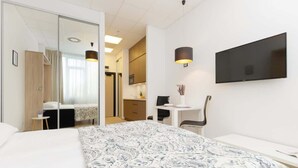 Une chambre d’hôtel avec un grand lit, un bureau, une chaise, un téléviseur fixé au mur et une porte coulissante donnant sur la salle de bain.