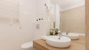 Une salle de bain moderne avec un meuble-lavabo en bois, deux vasques, des toilettes et un sèche-cheveux fixé au mur.