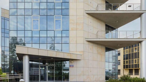 Un bâtiment moderne doté d’une façade en verre, d’une entrée couverte et d’une enseigne indiquant l’adresse, bien visible.