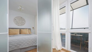 Un dormitorio con una cama, una lámpara fijada a la pared y un ventanal con vistas al exterior.