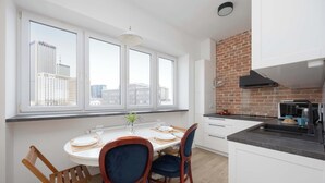 Una cocina moderna con armarios blancos, una pared de ladrillo decorativa y un ventanal con vistas a un paisaje urbano.