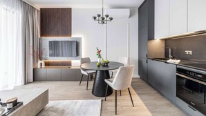 A modern kitchen with a built-in oven, a dining area with a round table and chairs, and a large flat-screen TV mounted on the wall. - Stylish Apartment in Wola | Balcony, Parking, Air Conditioning (Warszawa)