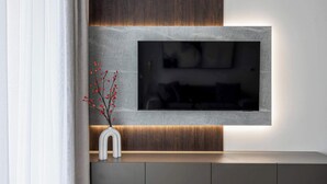 A modern living room with a flat-screen TV mounted on a wall with a wooden panel design. - Stylish Apartment in Wola | Balcony, Parking, Air Conditioning (Warszawa)