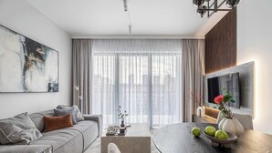 A modern living room with a grey sofa, a coffee table, and a dining table with decorative items. - Stylish Apartment in Wola | Balcony, Parking, Air Conditioning (Warszawa)