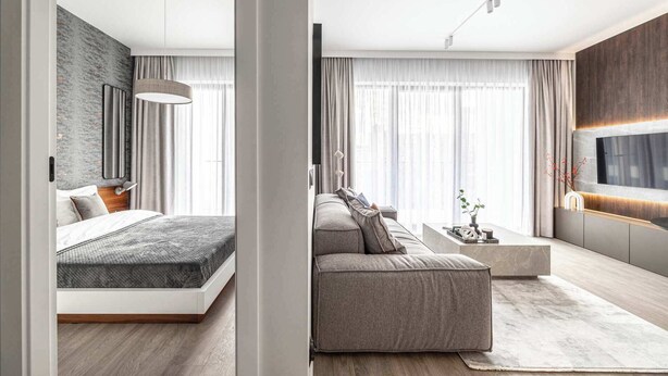 A modern hotel room with a bed, a sofa, a TV, and a large window with curtains. - Stylish Apartment in Wola | Balcony, Parking, Air Conditioning (Warszawa)