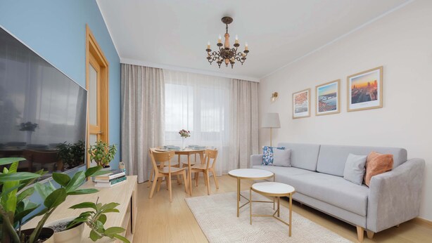 A modern living room with a sofa, a TV, a chandelier, and a dining area with a table and chairs. - Stylish Apartment in Warsaw | Smart TV and Workspace (Warszawa)