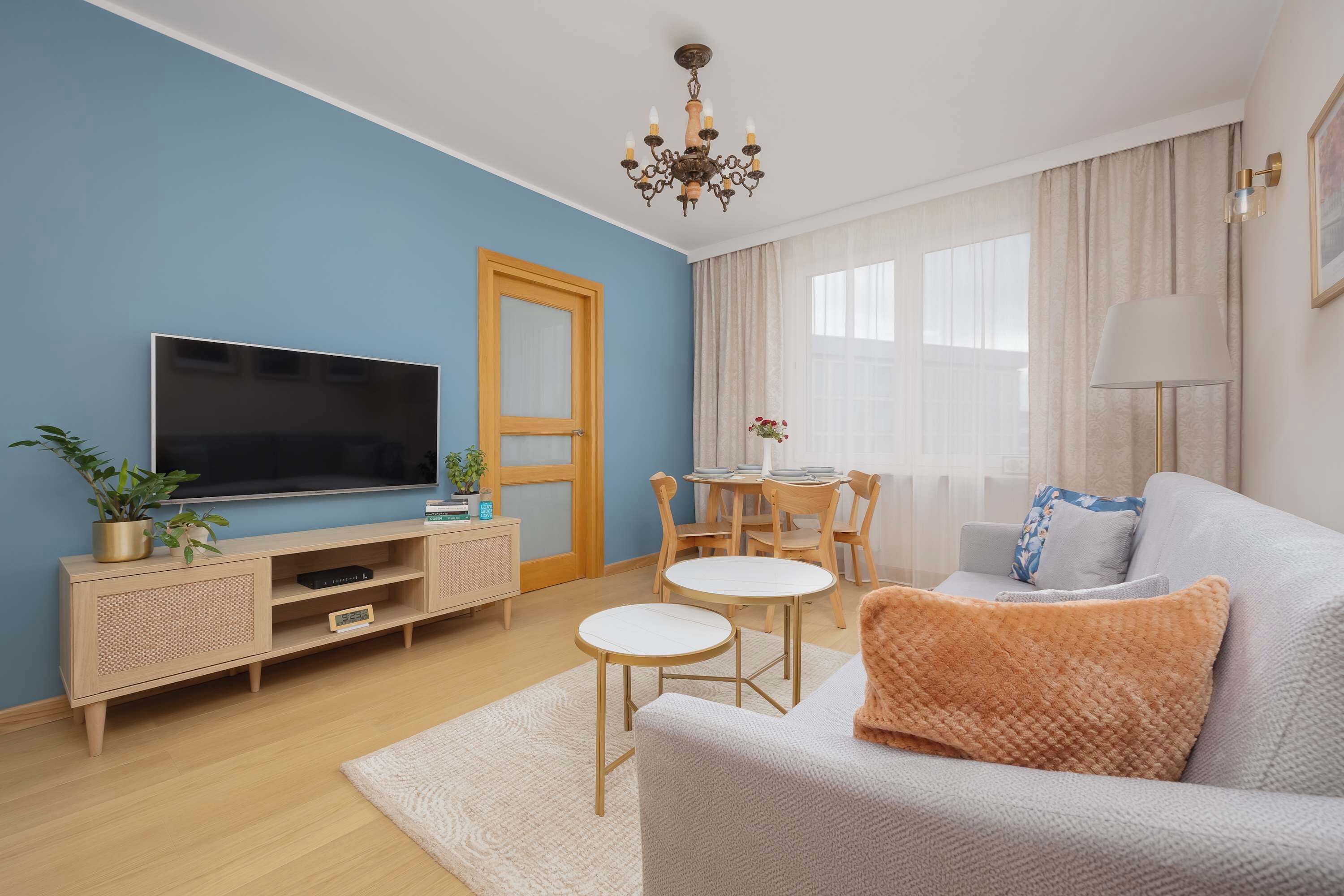 Una sala de estar moderna con una televisión de pantalla plana, un mueble de madera para entretenimiento, un sofá, una mesa de centro y un comedor con una mesa y sillas.