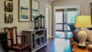 A living room with a wooden cabinet, a chair, a lamp, and a door leading to a balcony. - Jump Platform & Rope Swing, Dock. Kayak. Screened Porch. Firepit. Family Fun! (Dadeville)