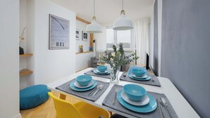 A modern dining area with a white table set for four, blue tableware, and a vase with greenery.