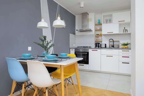 A modern kitchen with white cabinets, a black oven, and a wooden dining table with blue and yellow chairs.