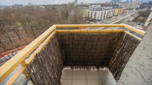 Un balcón con barandilla amarilla que da a una vista urbana con edificios y árboles desnudos.