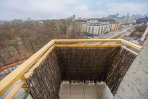 Varanda com guarda-corrimão amarelo com vista para um horizonte urbano, com edifícios e árvores sem folhas.